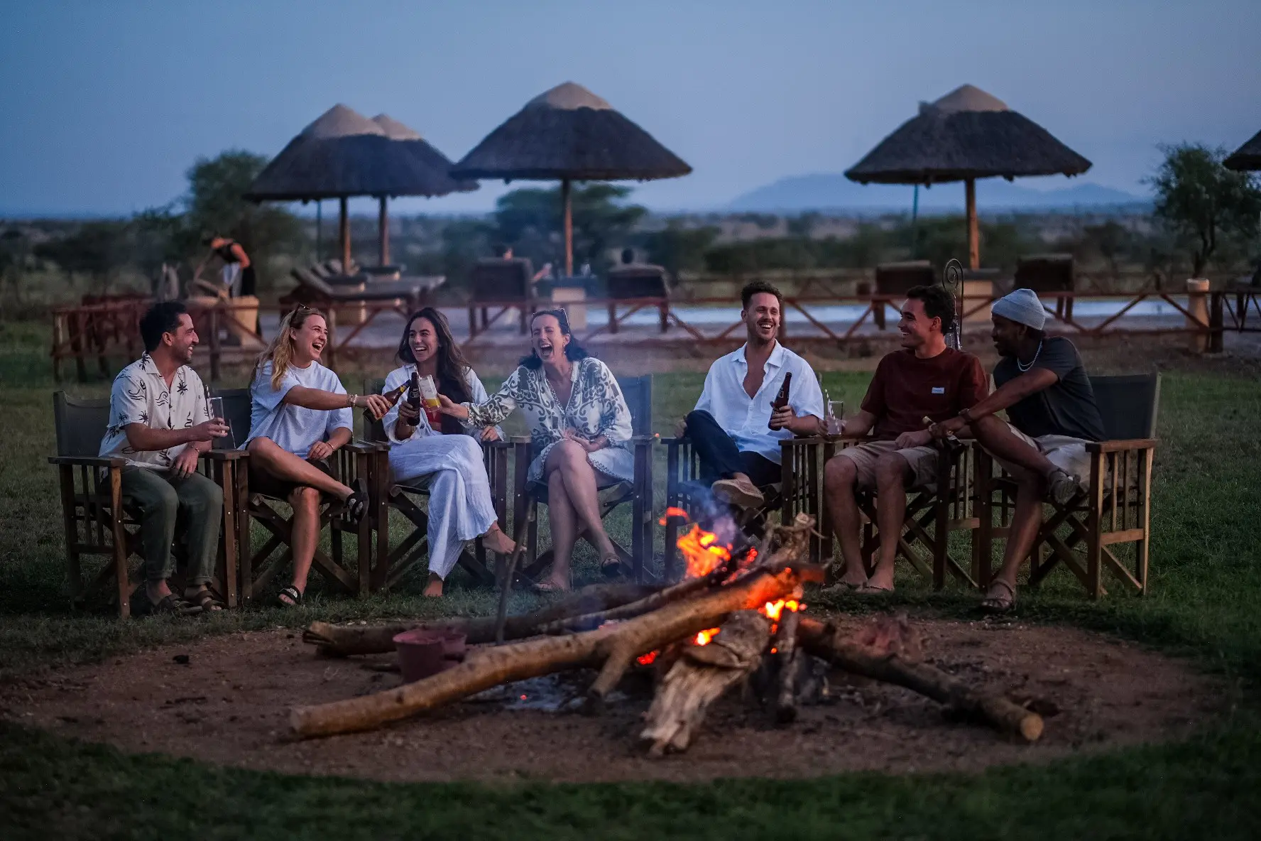 group of friends laughing around a campfire at dusk