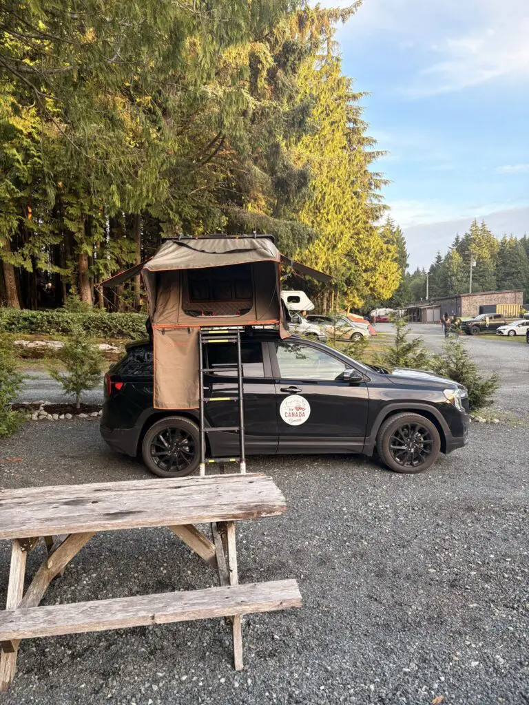 black car with rooftop tent and ladder at a campsite