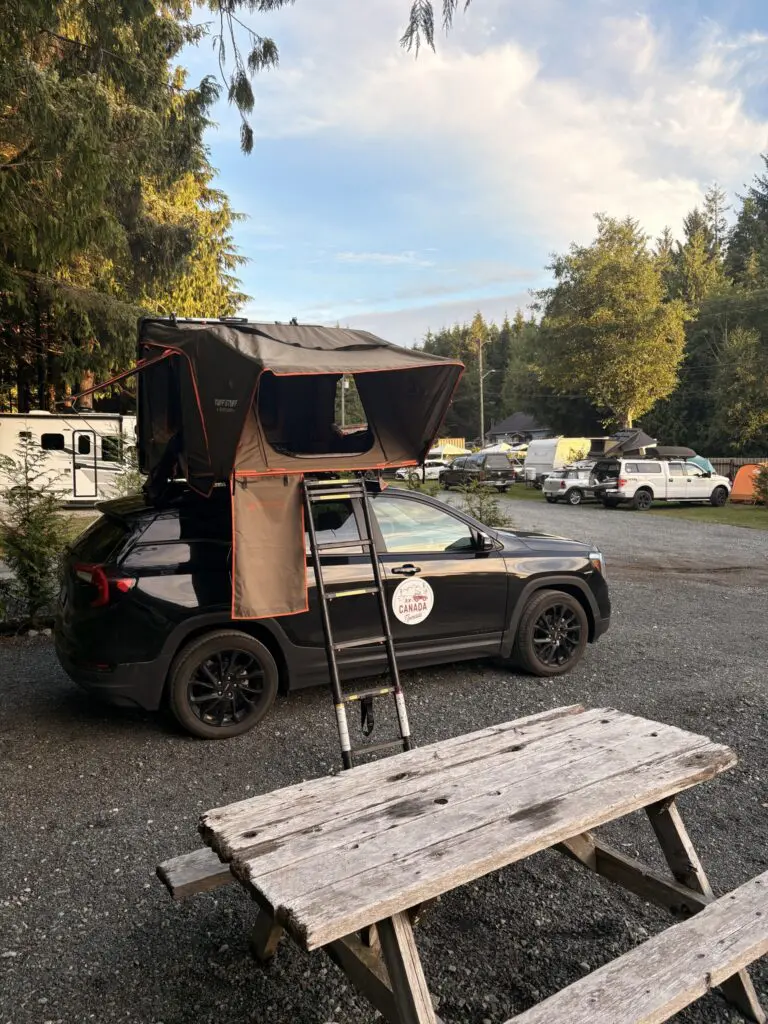black car with rooftop tent and ladder at a campsite
