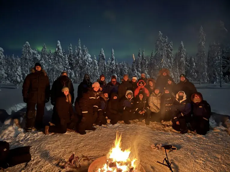 group of people by campfire under northern lights in Lapland