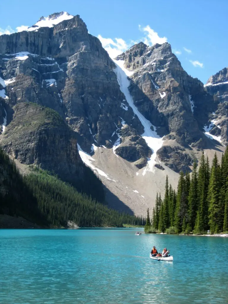 two people canoeing on turquoise lake with snowy mountains