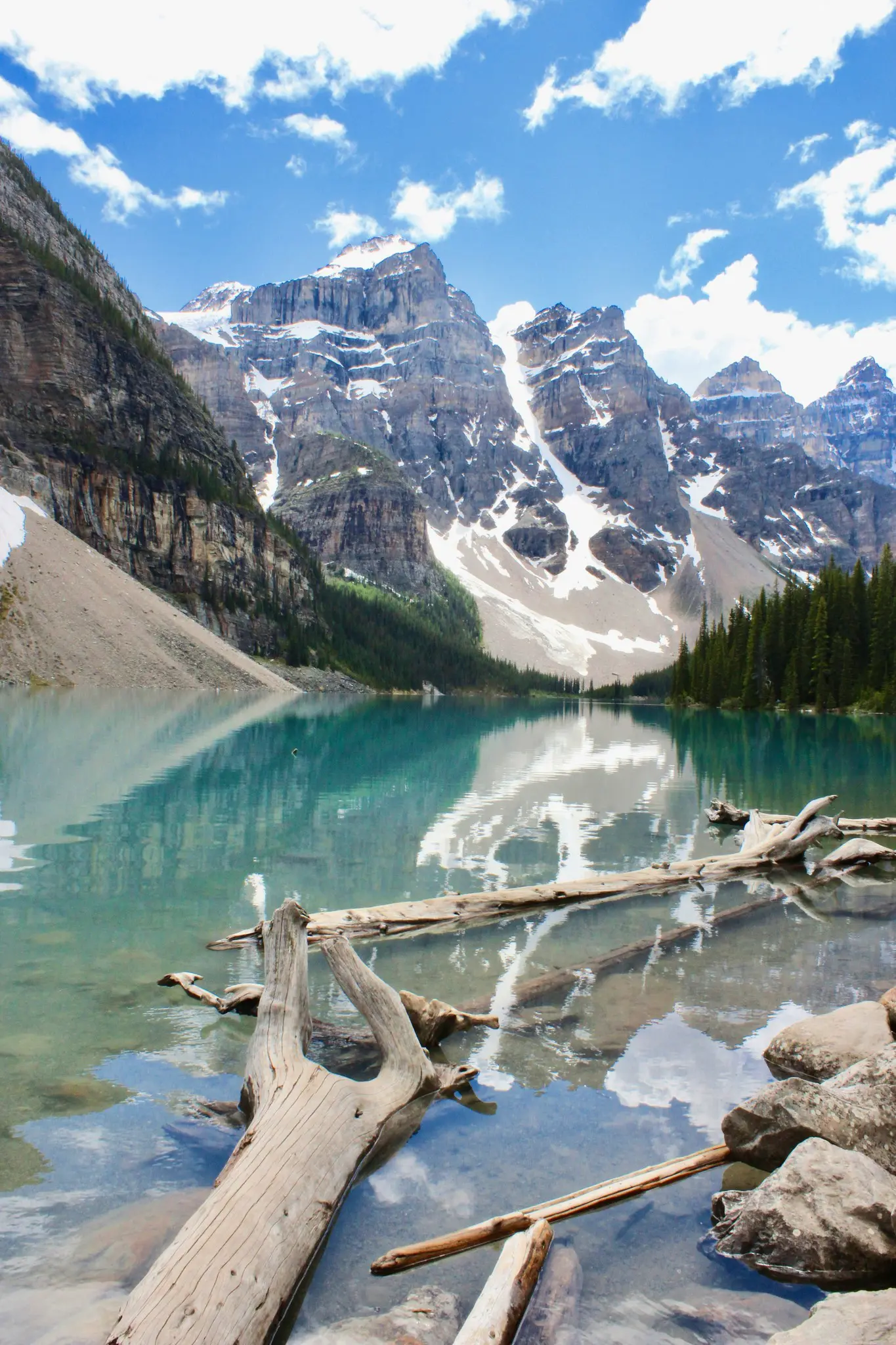 turquoise lake with snow-capped mountains and fallen logs