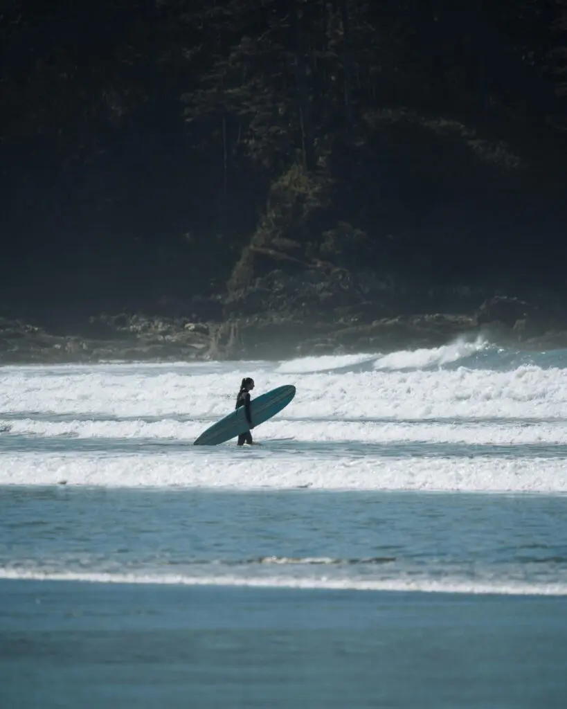 surfer walking into ocean with surfboard in Tofino, Canada