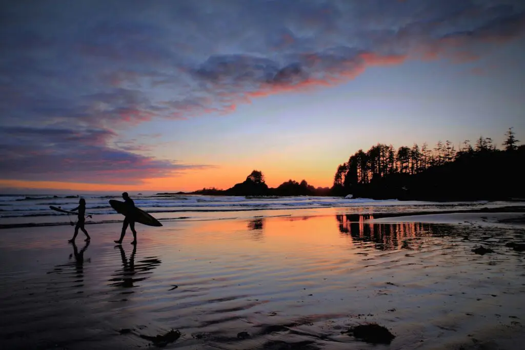 two surfers walking on Tofino beach at sunset