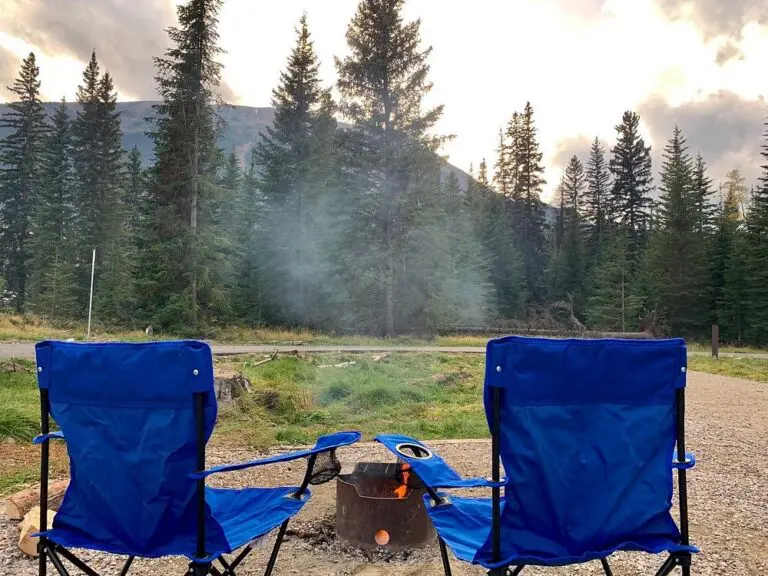 two blue camping chairs by a campfire in a forest