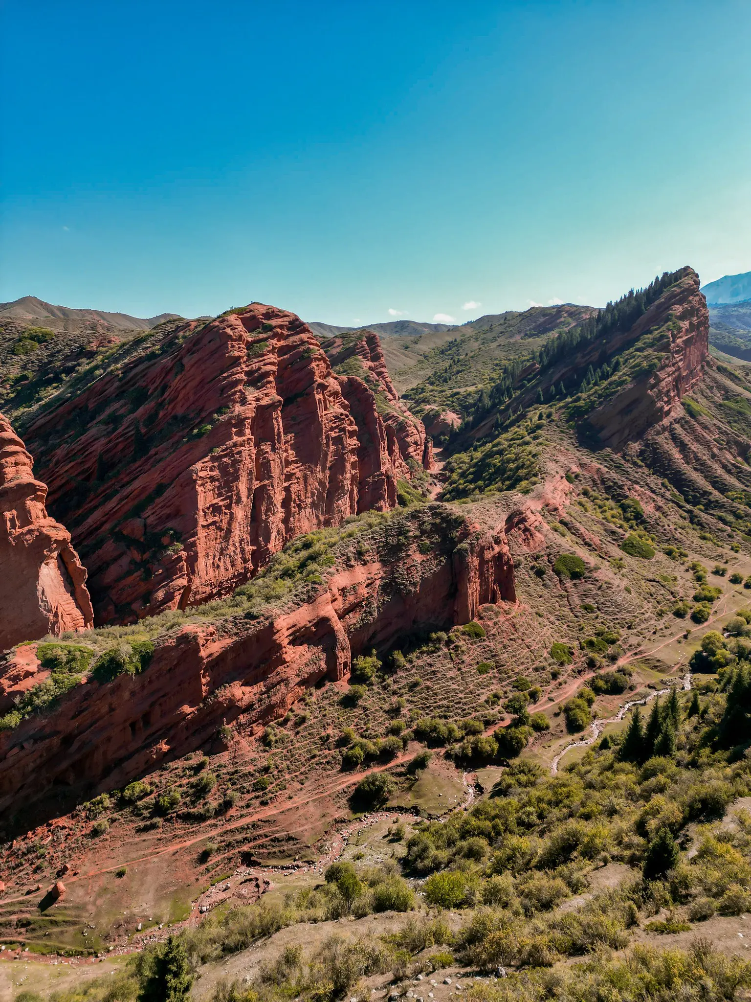 drone shot of red rock canyon and green hills under blue sky