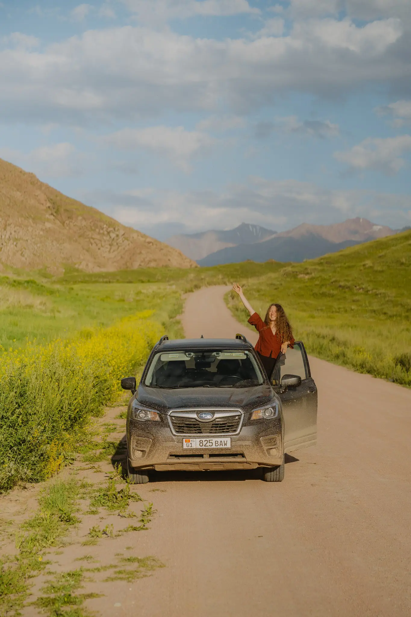 woman waving from car on dirt road in Kyrgyzstan mountains
