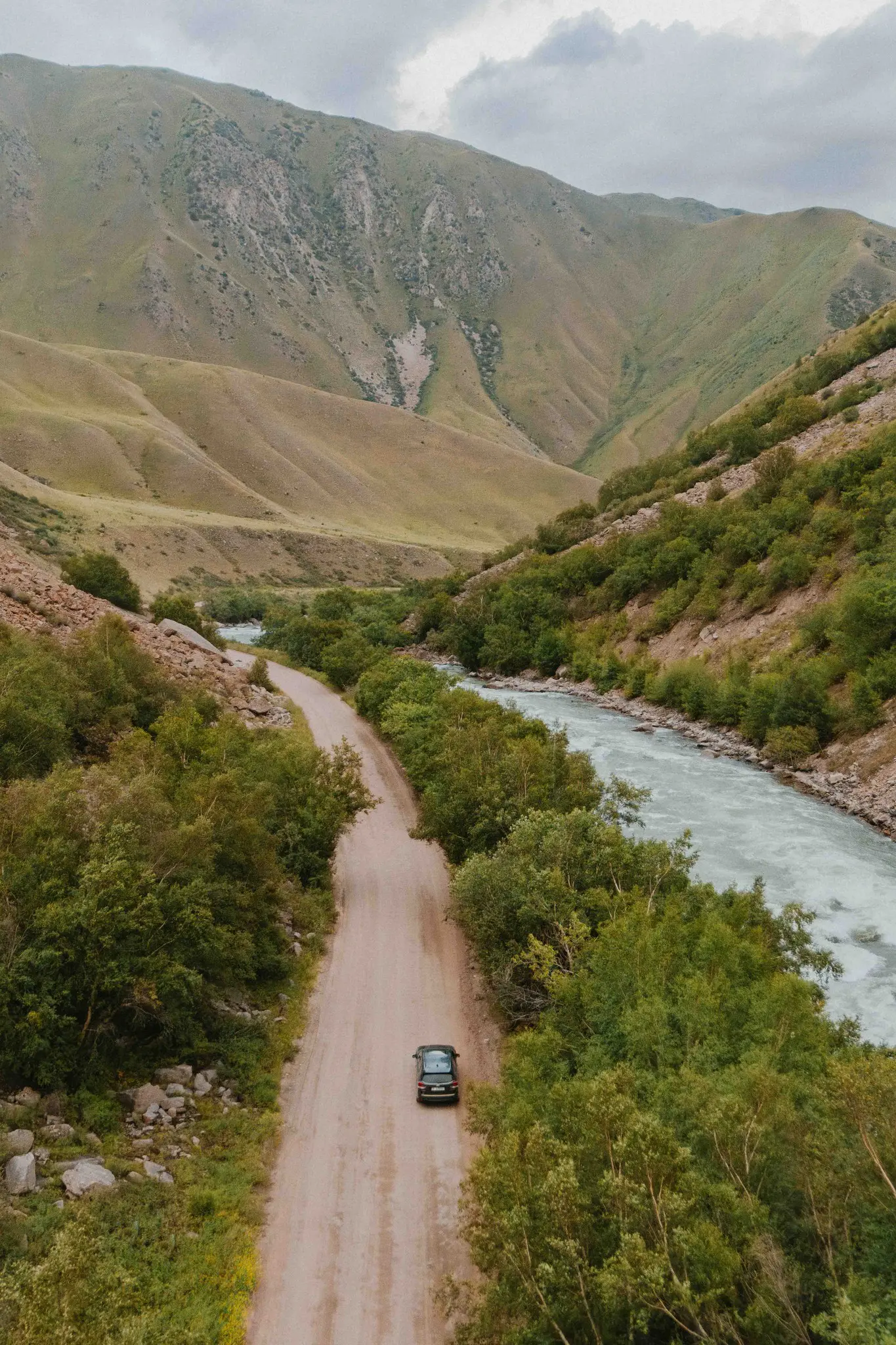 drone shot of a car driving on a dirt road in Kyrgyzstan mountains