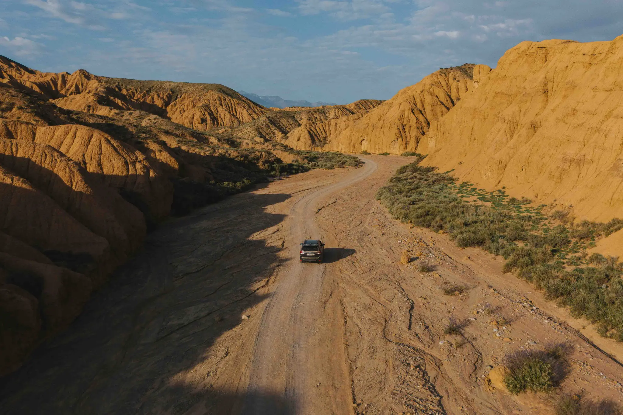 drone shot of a car driving on a dirt road through a desert canyon