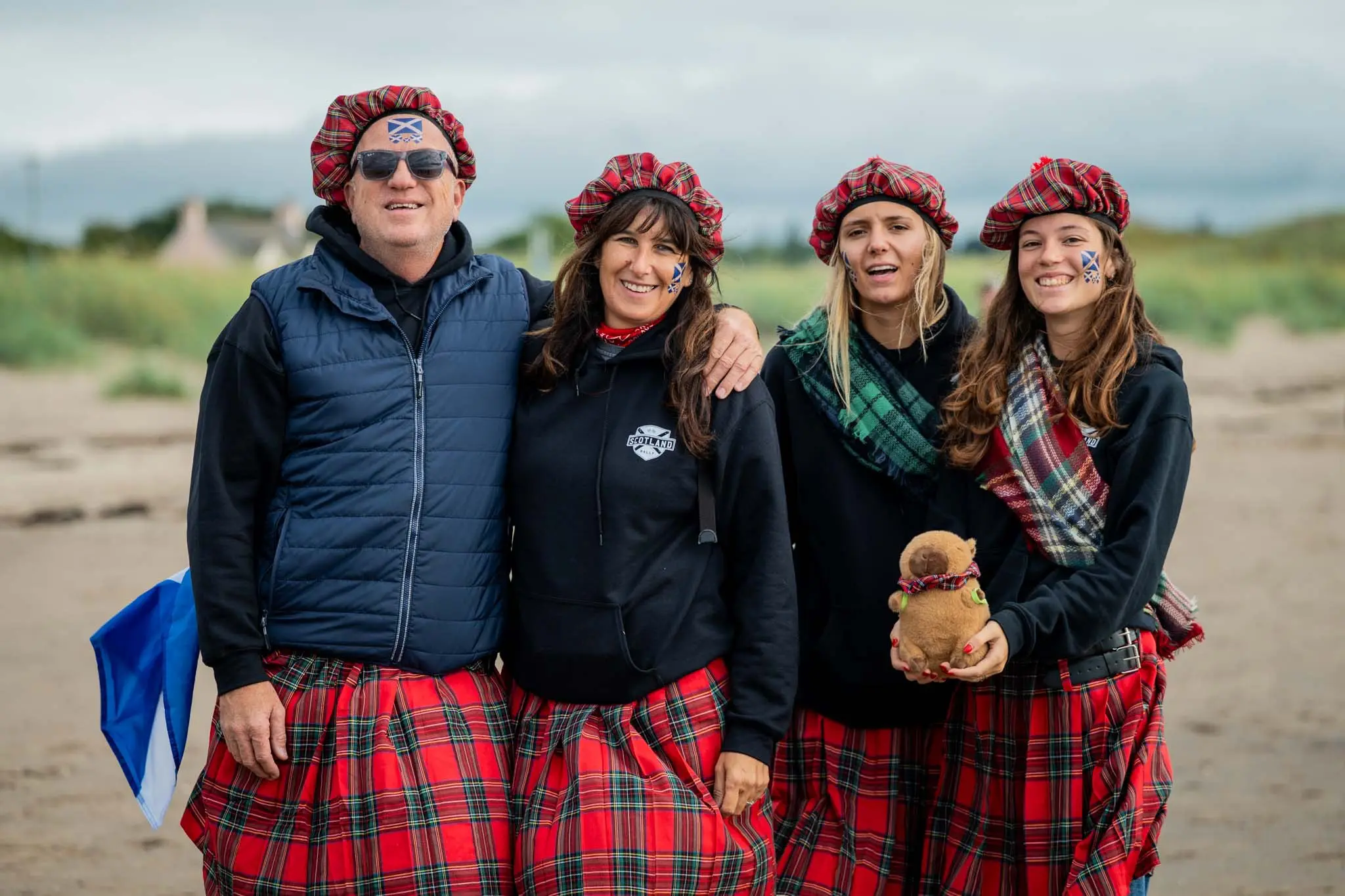 four people in kilts and tartan hats on a beach in Scotland