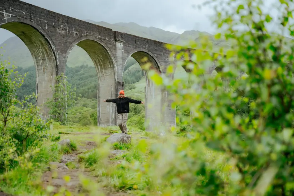 person balancing on rock under Glenfinnan Viaduct, Scotland