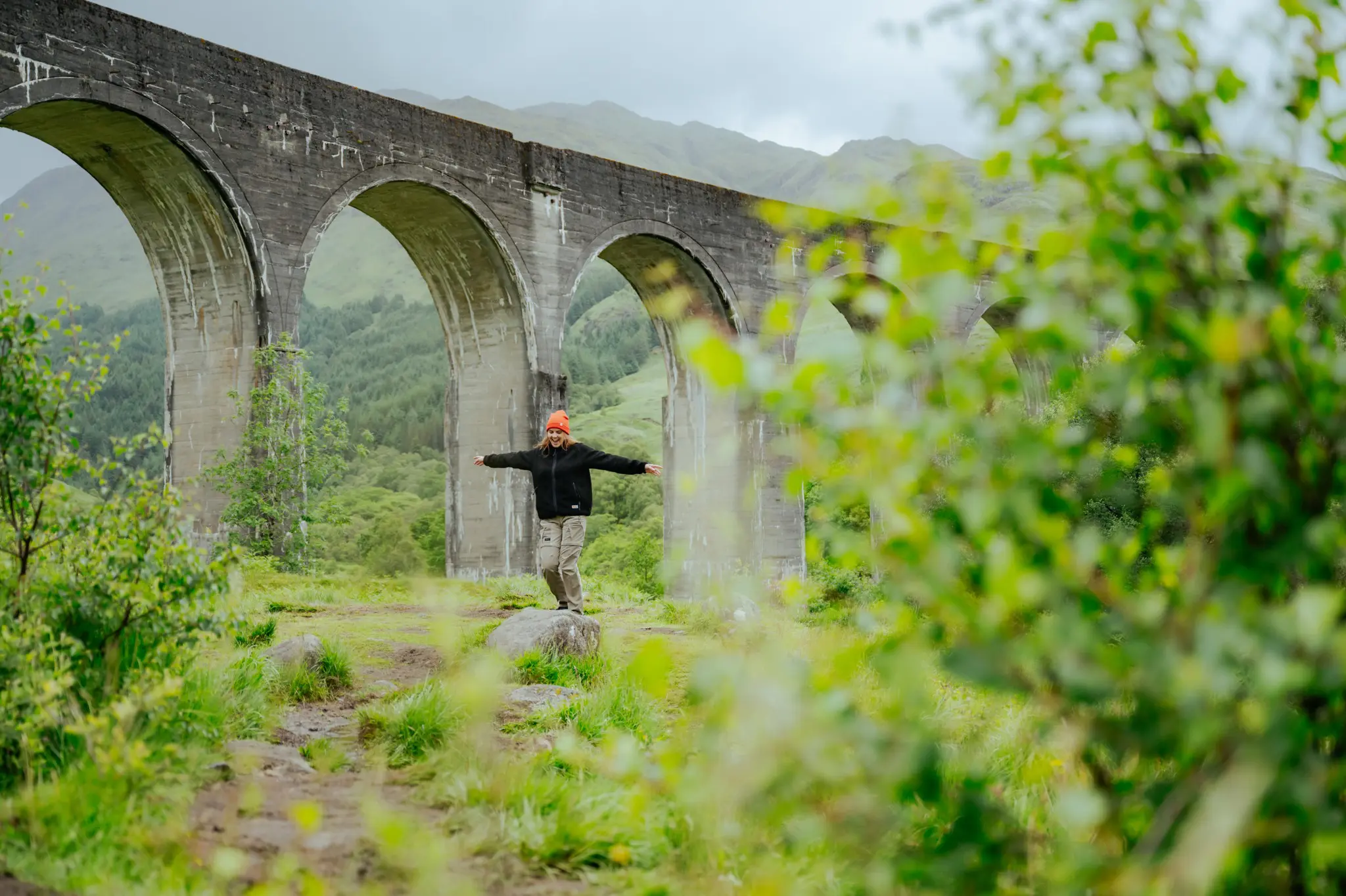 person balancing on rock under Glenfinnan Viaduct, Scotland
