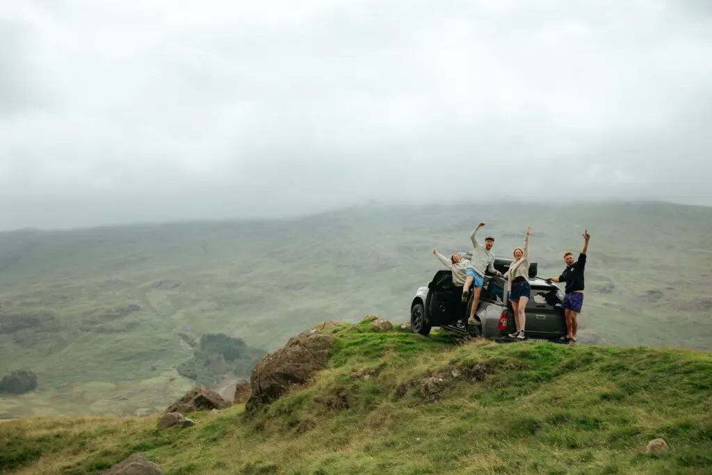 four friends celebrating on a car in the Scottish Highlands