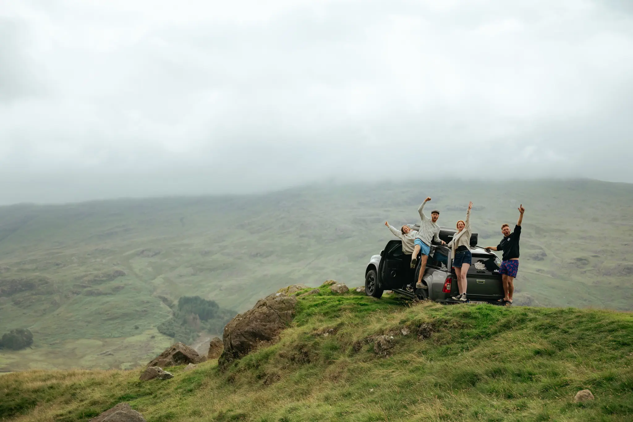 four friends celebrating on a car in the Scottish Highlands