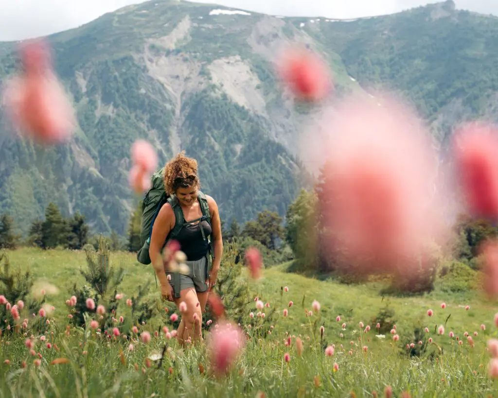 woman hiking through a field of pink flowers in the mountains