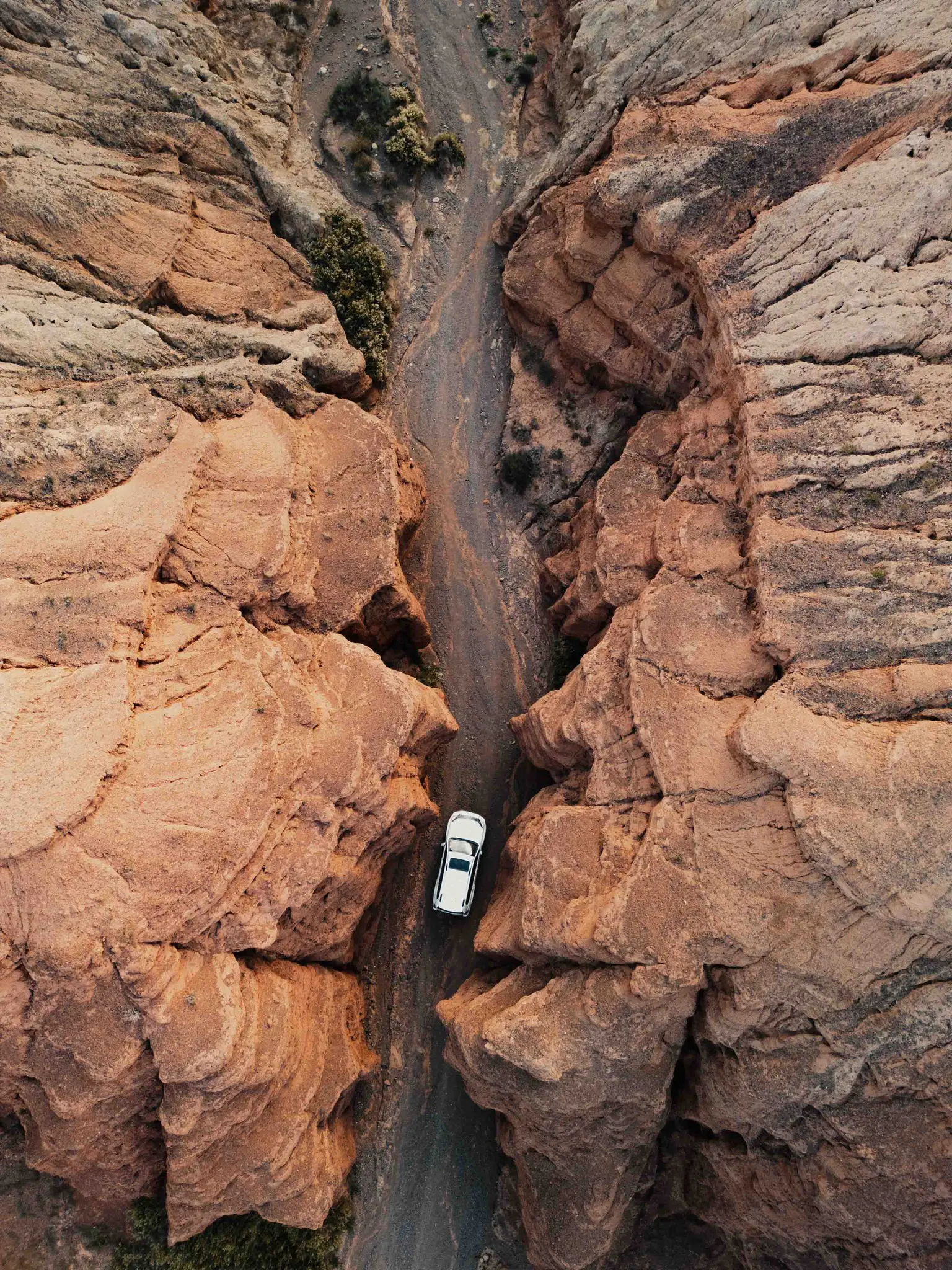 drone shot of white car driving through desert canyon